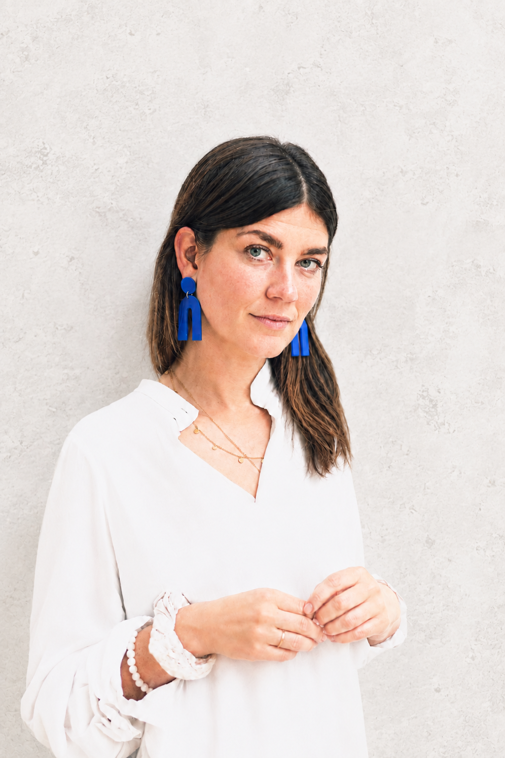 Christiane mit blauen Ohrringen vor einer hellen Betonwand